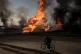 A man rides his bike past flames and smoke rising from a fir