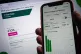 The OVO Energy app on a mobile phone is held against a laptop screen, March 26, 2023