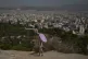 A tourist with an umbrella stands on Filopappou Hill as Athens stretches out in the background, Monday, July 7, 2025, while authorities in Greece impose mandatory work stoppages in parts of the country where temperatures are expected to exceed 40 degrees Celsius
