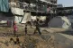A Palestinian woman carries buckets as she walks past tents for displaced people in a school used as a shelter in Gaza City, August 27, 2025