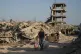 A displaced Palestinian man carries his belongings as he walks past destroyed buildings in the heavily damaged Sheikh Radwan neighborhood in Gaza City, October 11, 2025