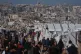Palestinians walk along a street past a tent camp, backdropped by buildings destroyed during Israeli air and ground operations in Gaza City, December 17, 2025