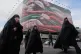 Women cross a street under a huge banner showing hands firmly holding Iranian flags as a sign of patriotism, as one of them flashes the victory sign, in Tehran, Iran, Wednesday, Jan. 14, 2026