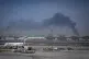 A plume of smoke caused by an Iranian strike is seen in the background as Emirates planes are parked at Dubai International Airport after its closure in Dubai, United Arab Emirates, Sunday, March 1, 2026