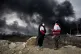 Two women from the Iranian Red Crescent Society stand as a thick plume of smoke from a US-Israeli strike on an oil storage facility late Saturday rises in the sky in Tehran, Iran, March 8, 2026