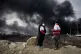 Two women from the Iranian Red Crescent Society stand as a thick plume of smoke from a U.S.-Israeli strike on an oil storage facility late Saturday rises in the sky in Tehran, Iran, March 8, 2026