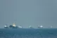 Cargo ships, including bulk carriers and general cargo vessels, sit at anchor offshore as a small motorboat passes in the foreground, in the Strait of Hormuz off Bandar Abbas, Iran, May 4 , 2026