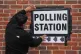 A man erects a polling station sign during the 2026 local elections directing voters to a portable cabin located in Armitage Road, in Greenwich, May 7, 2026