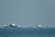 Cargo ships, including bulk carriers and general cargo vessels, sit at anchor offshore as a small motorboat passes in the foreground, in the Strait of Hormuz off Bandar Abbas, Iran, May 4, 2026