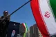 A woman waves an Iranian flag during a pro-government campaign as a portrait of the slain Supreme Leader Ayatollah Ali Khamenei, who was killed in US and Israeli strikes on February 28, is displayed behind her, Tehran, Iran, June 15, 2026