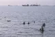 Residents swim as cargo and commercial vessels are anchored in the Strait of Hormuz off Bandar Abbas, Iran, August 6, 2026