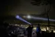 A Palestinian scans a valley with a flashlight as cars move on the top of a hill during a volunteer night watch to help prevent Israeli settler attacks in the West Bank town of Sinjil
