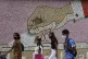 Youths walk past a mosaic mural with the image of a hand dep