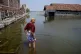 A man walks on a flooded pathway outside his house in Timbul