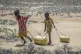 Young girls pull containers of water as they return to their