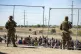 People wait in line adjacent to the border fence under the w