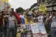 A protestor holds a poster board with the prices of basic fo