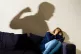 A shadow of a man with a clenched fist as a woman covers in 