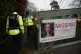 Police officers walk past a missing person appeal poster for