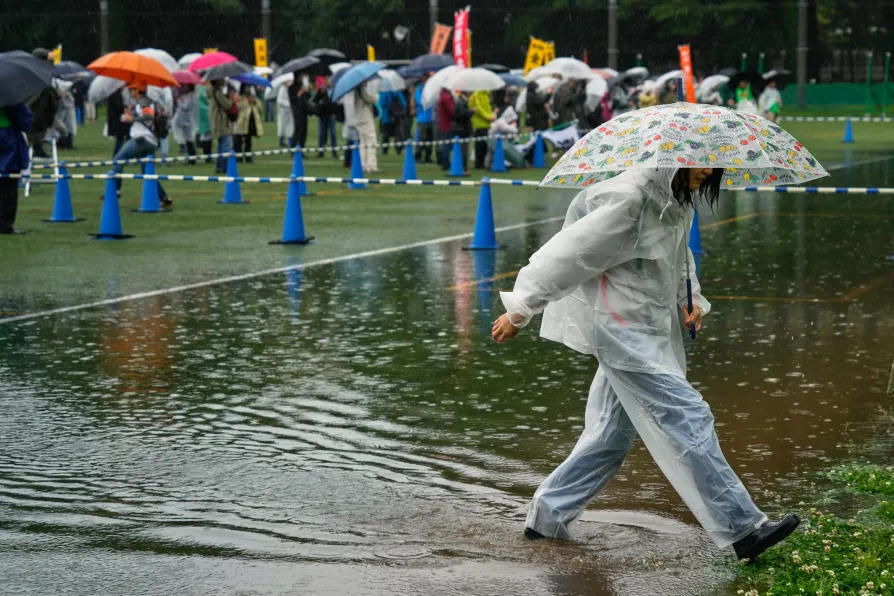 One of union members carefully steps through rain-formed puddles to participate in a May Day rally in the rain Friday, May 1, 2026, in Tokyo